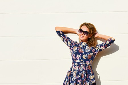 Beautiful and happy young woman standing against wall. Wearing sun glasses.の写真素材