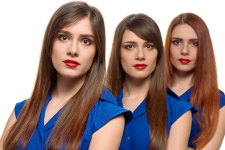 studio portrait of three young beautiful women. triplets. one girl is front of others on white background. they are very similarの写真素材