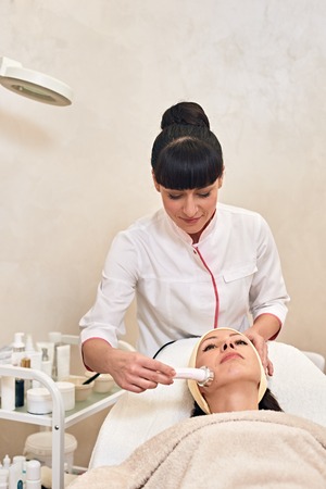 cosmetologist doing phonophoresis skin for young woman in salon. top-view side-viewの写真素材