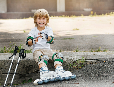 Little boy puts rollers sitting on the roadside. pull on protective gloves