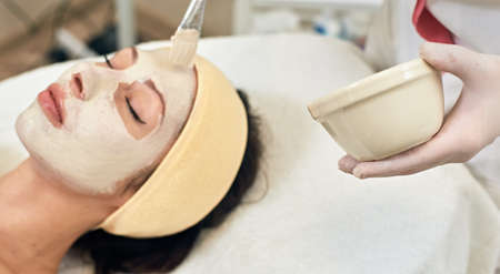 container with mask is on focus and young beautiful woman with facial mask are background, spa treatmentの写真素材