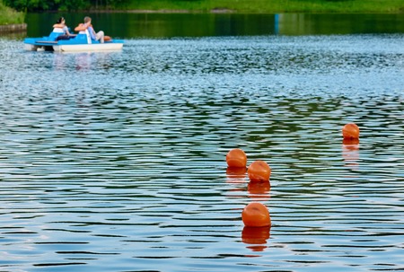 several red buoys on calm lake water, pedal boats in distanceの写真素材