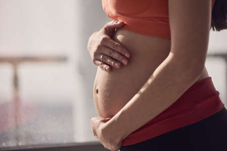 Young pregnant woman sitting on floor, part of body