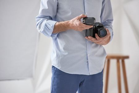 Closeup of young man holding digital camera with synchronizer in studio, focus is on synchronizerの写真素材