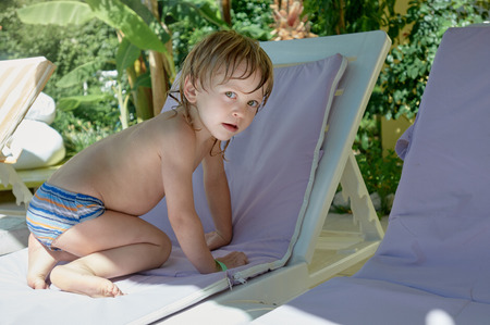Cute little boy sitting on chaise-longue near swimming poolの写真素材