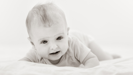 Portrait of cute newborn baby lying on belly at home, black white image with bit toningの写真素材