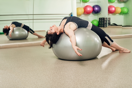 Athletic relaxed woman exercising with fitball in modern gymの写真素材