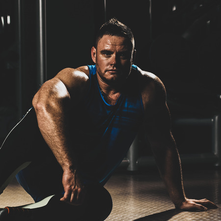 Portrait of strong handsome sporty man sitting on floor in gym, with color imitating social network filterの写真素材