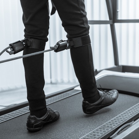 Closeup photo of man walking on treadmill with electrodes on his legs black white image with a blue...