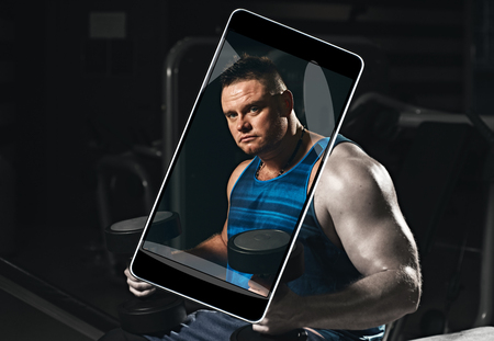 Smartphone displaying photo of muscular young bodybuilder with dumbbells at gymの写真素材