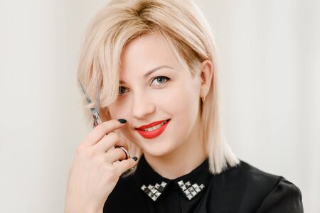 Beautiful blonde female hairdresser holding professional scissors