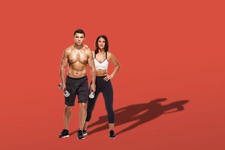 Healthy couple with dumbbells on red background with shadow on floorの写真素材