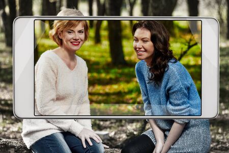 Pretty happy girlfriends in autumn park, smart device concept