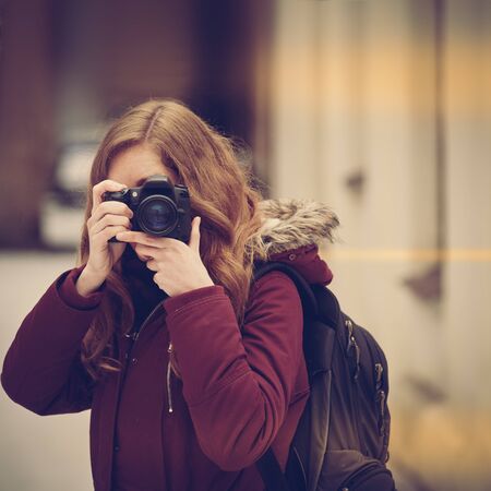 Young attractive woman photographer taking photos in winter city, image with warm vintage toning