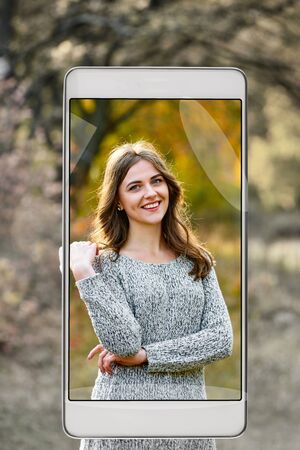 Portrait of young attractive woman in autumn park, demonstration of device capabilities