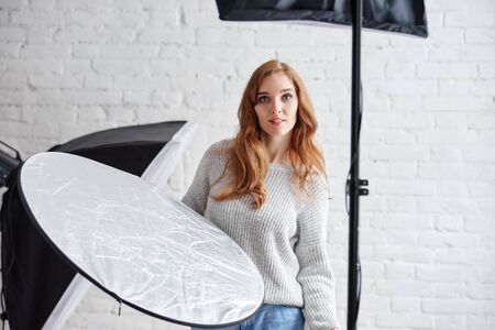 Attractive professional female photographer holding reflector during photo session