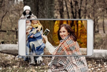 Young woman making photo of her friends in park, smart device conceptの写真素材