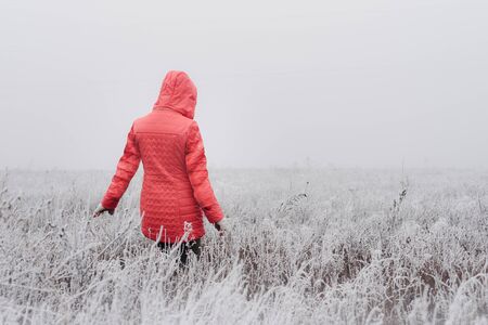 Woman in red coat walking in frosty field on foggy dayの写真素材