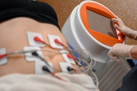 Closeup of professional cosmetologist doing myostimulation procedure on belly for female client