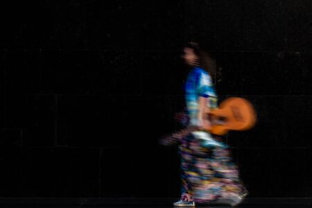 Stylish woman walking with guitar. Long exposure, intentional camera shake to introduce an...