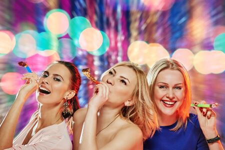 Portrait of three happy pretty girlfriends with carnival whistles celebrating partyの写真素材
