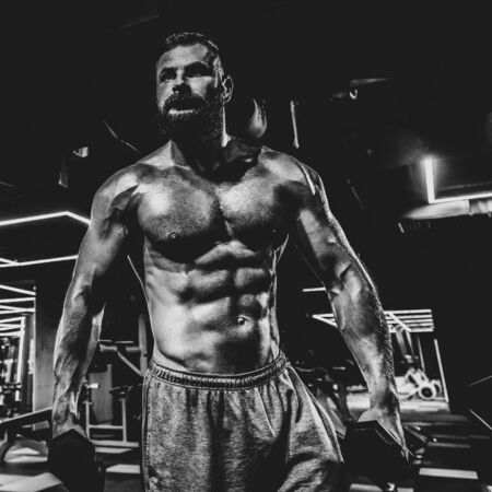 Portrait of strong handsome fit man exercising in gym with dumbbells, dramatic black and white imageの写真素材