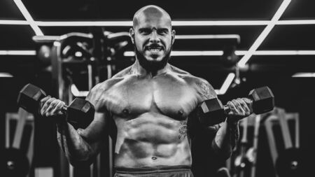 Handsome strong bodybuilder doing heavy weight exercise with dumbbells, dramatic black and white imageの写真素材