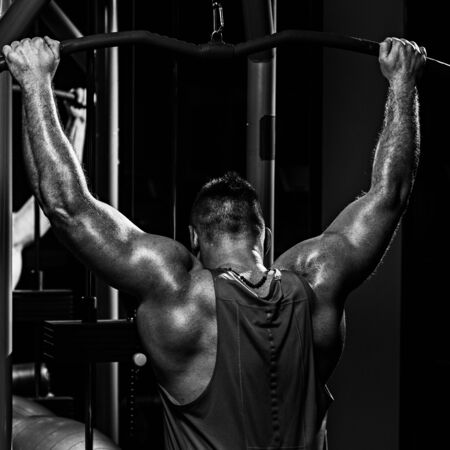 Back view photo of strong healthy weightlifter training in gym. dramatic black white image