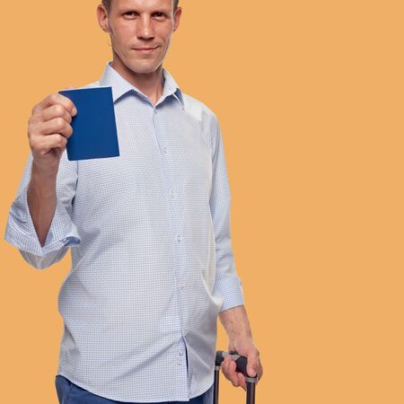 Happy male tourist with passport and bag going abroad for vacation on orange skin color backgroundの写真素材