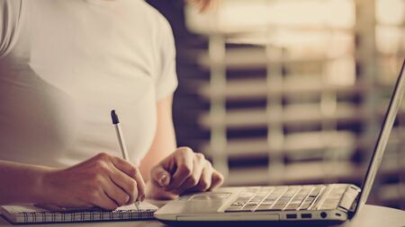 close up of Young businesswoman sitting in modern office with laptop and taking notes in notebookの写真素材
