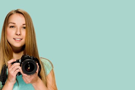 Beautiful young woman with camera taking images on emerald green background