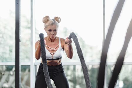 Strong attractive woman exercising with battle rope in gym