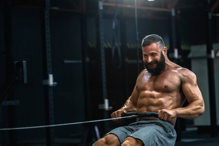 Young strong bearded bodybuilder doing low cable pulley row seated