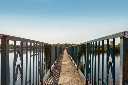 Old metal footpath bridge on river over blue sky backgroundの写真素材