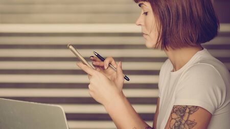 Young female content writer using smartphone for chatting with clients
