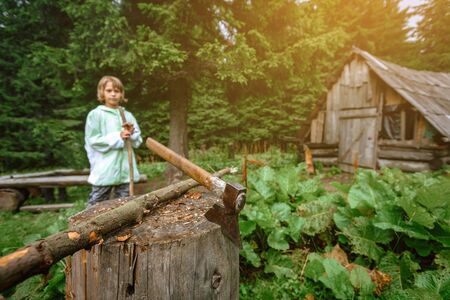 Young teenager boy standing near axe in Carpathian village, supervision for kids conceptの写真素材