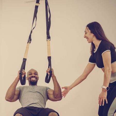 Attractive young woman and handsome african man training together with elastic band