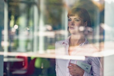 Portrait of beautiful minded businesswoman looking on window and dreaming about future projectの写真素材