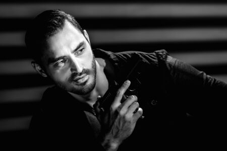 Monochrome portrait of brutal handsome mafia man holding gun