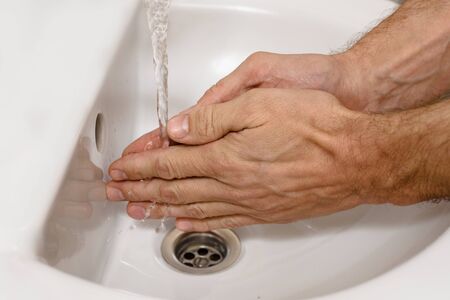Closeup photo of man washing his hands with at bathroom sink