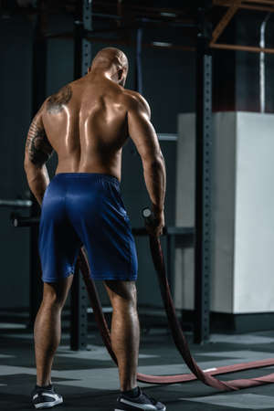 Back view of fit sporty man training with battle ropeの写真素材