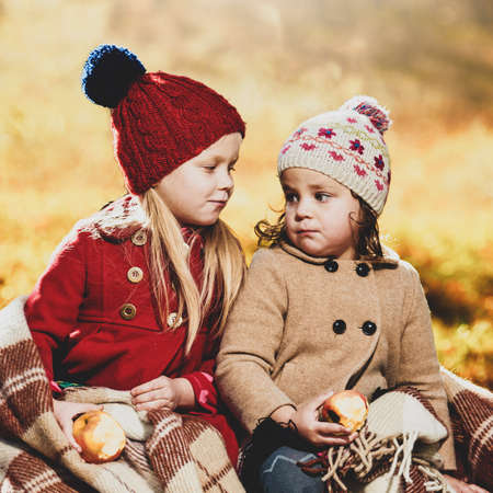 Portrait of two smiling little sisters eating apples in autumn parkの写真素材