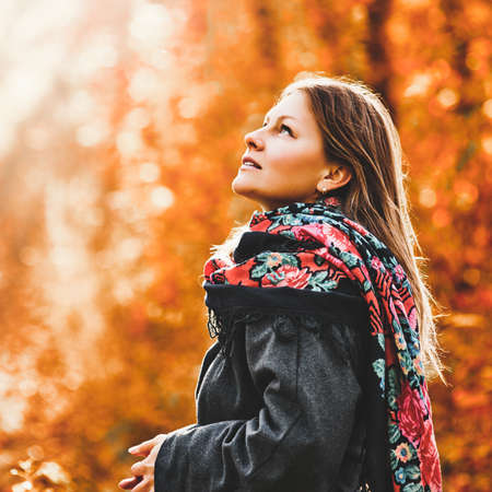 Portrait of beautiful smiling woman posing in autumn forest with cup of teaの写真素材