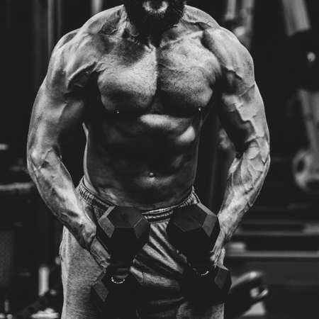 close up of Muscular athletic bodybuilder working hard in gym on dark background, dramatic black and...