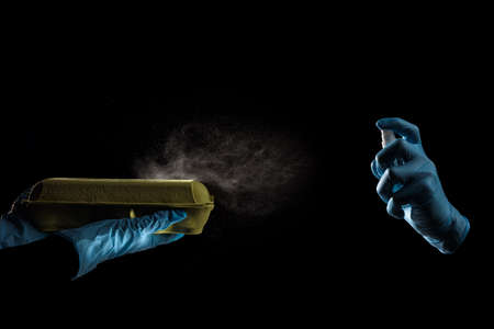 People in medical gloves using antibacterial spray to remove virus off container with eggs
