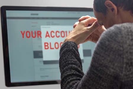 Upset minded man reading text Your account blocked on computer screenの写真素材