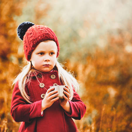Portrait of cute little girl holding cup of tea in autumn park