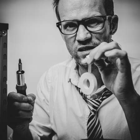 Black and white photo of Sad man applying plaster on finger after fixing broken computer in officeの写真素材