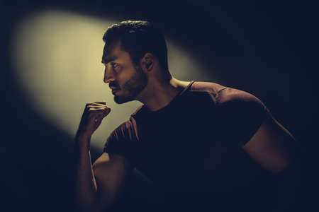 Profile view of serious athletic man dreaming on dark background