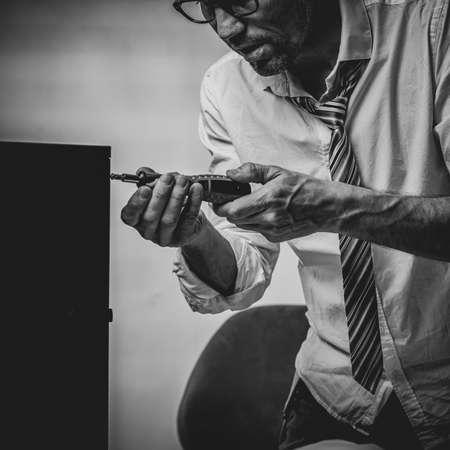 Black and white photo of Unqualified tired office worker repairing broken computer